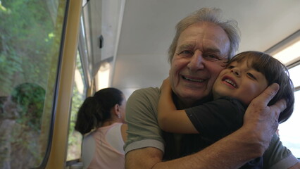 Grandfather and grandson embrace while traveling by train. Grandparent hugging grandchild inside railroad transportation seated by window. Generational love concept