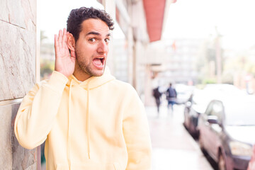 young hispanic man looking happy, listening, trying to hear a secret conversation or gossip,...