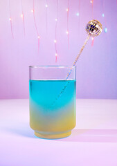 A Pastel Spring Cocktail: A Multi-Color Blue and Gold Disco Ball Swizzle Stick with Festive Party Lights on a Purple Background,  Spring Party, Club, Bar, Nightlife, Disco Concept