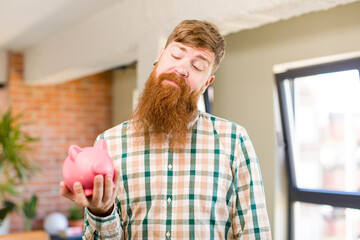 red hair man smiling and looking with a happy confident expression with a piggy bank