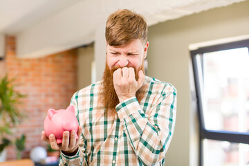 red hair man feeling scared, worried or angry and looking to the side with a piggy bank