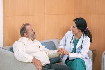 Obraz premium Female doctor in white medical coat and patient discussing something, holding his hand and smiling while sitting on sofa. Medicine and health care concept. Doctor and patient.