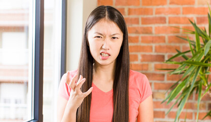 asian pretty woman at home against brick wall with a plant