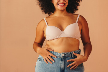 Happy young woman wearing a bra and jeans in a studio - obrazy, fototapety, plakaty