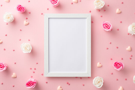 Mother's Day concept. Top view photo of photo frame white and pink rose buds small hearts and sprinkles on isolated pastel pink background with copyspace