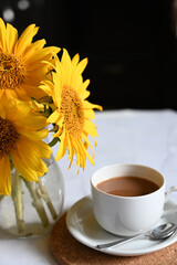 Morning coffee. Cozy composition: a cup of coffee on an open book, a blue sweater and sunflower flowers on a concrete background. Still life concept. Copy space.