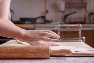 An interesting perspective on the process of making Italian pasta at home. Beautiful hands sprinkle flour and smooth the dough on the table at home. Cook at home. real people. atmospheric photo