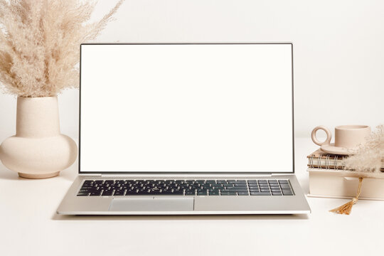 Mockup laptop with white screen on the table with vase, pampas grass and decorations. Aesthetic background for study, cozy home office, promotion, social media