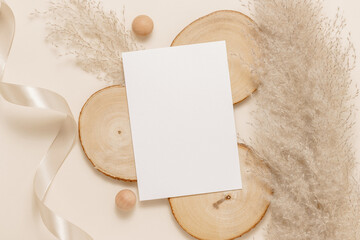 Blank paper sheet card on wood with pampas grass and ribbon, neutral beige background. Aesthetic gentle mockup card for wedding, greeting and invitation, logo and design. Top view, flat lay