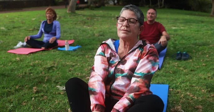 Senior people doing yoga meditation outdoor with city park in background - Healthy lifestyle and joyful elderly lifestyle concept