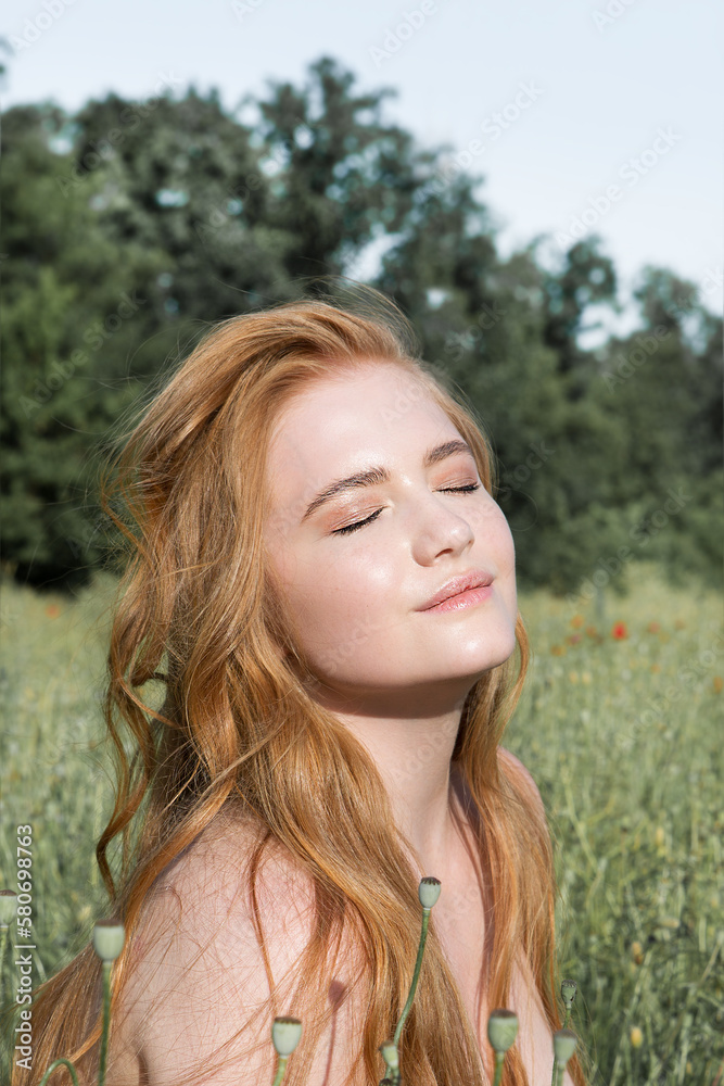 Wall mural young beautiful woman is resting in the rays of the sun sitting in the grass on the field.