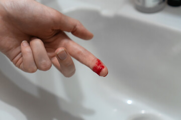 Close-up of a woman's cut finger in blood over the sink