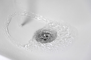 Close-up of a stream of clean water flowing into a clean white ceramic sink.