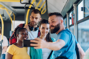 Multiracial friends taking a selfie with a a smartphone while riding a bus in the city