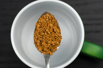 Close-up of a teaspoon with granulated instant coffee over a mug, macro. Top view