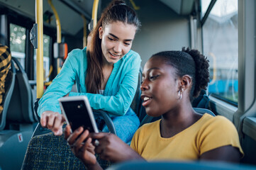 Multiracial female friends using a smartphone while riding a bus in the city