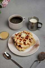 Homemade of tasty Waffles Plate, Caramel Sauce, Coffee Cup, Milk on a Grey Background