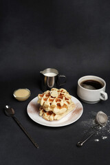 Homemade of Breakfast tasty Waffles, Caramel Sauce, Coffee Cup, Milk, dessertspoon, strainer on a Black concrete Background