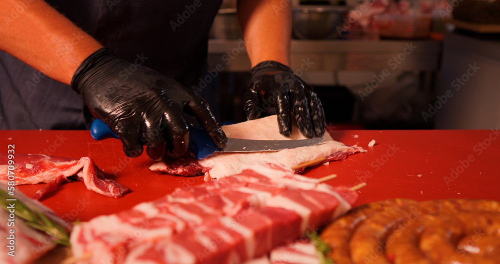 Wall mural Butcher with black gloves cutting raw lamb loin chops. Uncooked lamb chops on wooden cutting board table. Concept of fresh raw meat.