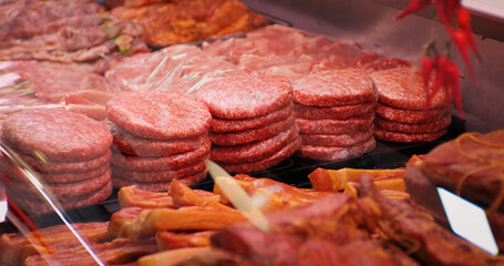 Burger cutlets on display in butchers shop vitrine made of beef meat. Row of beef burgers in a showcase in supermarket. Food industry concept.