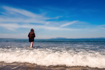Teenager girl in dark t shirt in the ocean, Blue cloudy sky in the background. Summer time and holiday mood. Enjoy open fresh water and play with waves concept. Irish beach with stunning view.