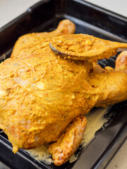 Raw uncooked full chicken on a metal cooking tray in yellow lemon and mustard marinade ready to be cooked in an oven. Fresh poultry product.