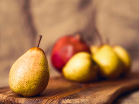 Still life with ripe pears and pomegranate on a wooden board and hessian cloth background. Selective focus. Soft and dreamy look.