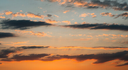 Obraz premium An unbelievably beautiful summer sunset. Yellow-orange clouds against a barely blue sky. The sun's rays from below illuminate the clouds. The beauty of nature. A summer sunset.