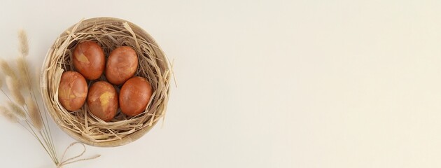 Happy Easter banner, brown eggs painted with onion peel, rural composition with wooden bowl and straw, bunny tail grass. - Powered by Adobe