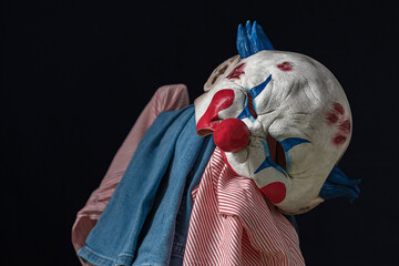 A shirt and jeans hang from the back of a chair, with a creepy clown mask on top. The dressing room...