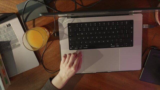 Top view of woman hands using graphic pen, working by laptop, pressing hot keys, working or studying online, table with lots of stuff, plant, glass of juice, tech devices. High quality 4k footage