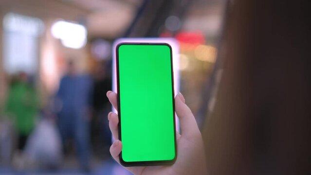 A young girl holds a phone with a green screen. Mall. Use green screen for copy space closeup. Chroma key mock-up on smartphone in hand. hold mobile phone and looking photos or pictures