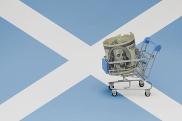 Metal shopping basket with dollar money banknote on the national flag of scotland background. consumer basket concept. 3d illustration