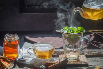 Pouring tea from a teapot into a cup of hot tea cane sugar dry tea leaves and mint herb.selective...
