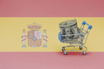 Metal shopping basket with dollar money banknote on the national flag of spain background. consumer basket concept. 3d illustration