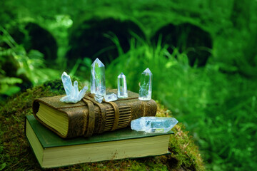 witch spell book and clear quartz minerals on natural forest background. Gemstones for healing...