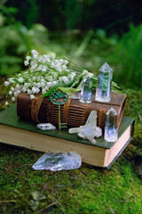 witch book, key, spring flowers and clear quartz minerals on natural forest background. Gemstones...
