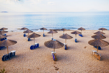 Tranquil beach morning, with a peaceful horizon over the sea and parasol-covered chairs in the...