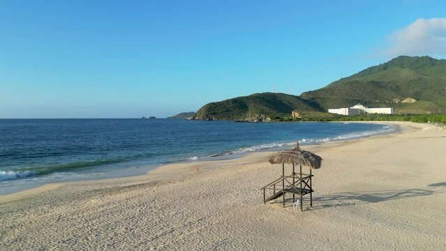 A wooden lifeguard tower with a straw roof on the beach at dawn. Deserted tropical shore and mountains in the background. Playa Puerto Cruz, Venezuela