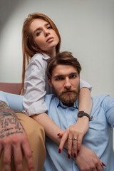 Cool fashion beautiful young couple posing in the studio. Beautiful redhead model girl hugging brutal handsome hipster guy with beard and tattoo