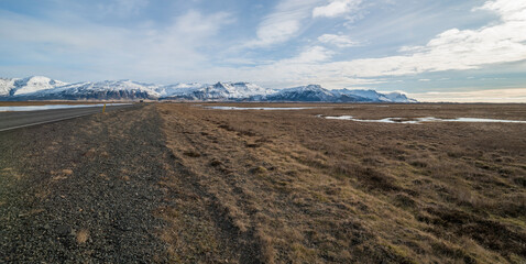 Amazing winter landschape in Iceland with the ringroad in the side, brown grassy fields and snowy mountains in the background during a sunny day in March.