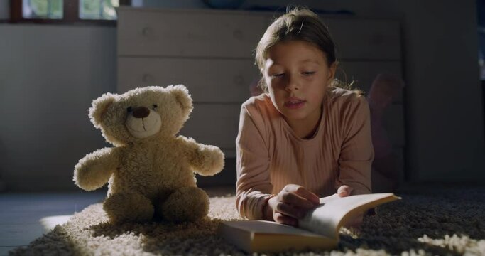 Portrait of a Little Female Child Reading a Book to her Favorite Teddy Bear During Evening. Happy Cute Girl Playing with her Toy, Telling a Story. Concept of Childhood with Cosy Atmosphere