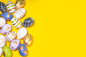Bright Easter greeting card background. Trendy colored black, golden, stripe painted Easter eggs with white bunny rabbits decor, tulip flower on high-colored yellow background, flat lay copy space