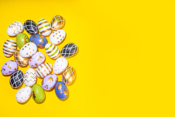 Bright Easter greeting card background. Trendy colored black, golden, stripe painted Easter eggs with white bunny rabbits decor, tulip flower on high-colored yellow background, flat lay copy space