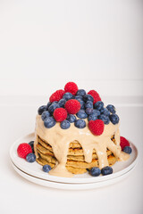 Delicious freshly cooked thick and fluffy gluten free pancakes stacked on white plate, served with cashew cream and fresh berries. Healthy food. Place for text.
