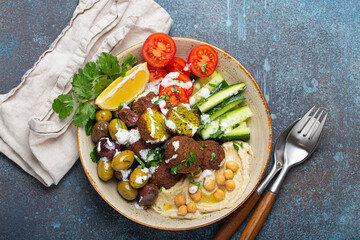 Falafel salad bowl with hummus, vegetables, olives, herbs and yogurt sauce. Vegan lunch plate top view on rustic stone background, healthy meal with falafel and veggies