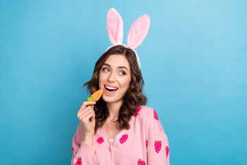 Obraz na płótnie Canvas Photo of funky dreamy lady dressed pink cardigan easter ears enjoying carrot biscuit empty space isolated blue color background