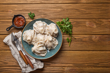 Georgian dumplings Khinkali on plate with red tomato sauce and fresh cilantro top view on rustic wooden background, traditional dish of Georgia, space for text