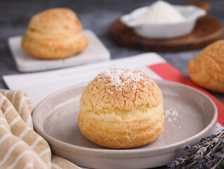 A French cream puff crack bun (Choux au Craquelin) in a plate, topped with grated coconut filling with another choux in background. It's a dessert base of savory choux dough bun 
