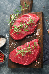 Raw beef steak. Marbled raw fresh Ribeye steak with rosemary, salt and pepper on cutting board on...